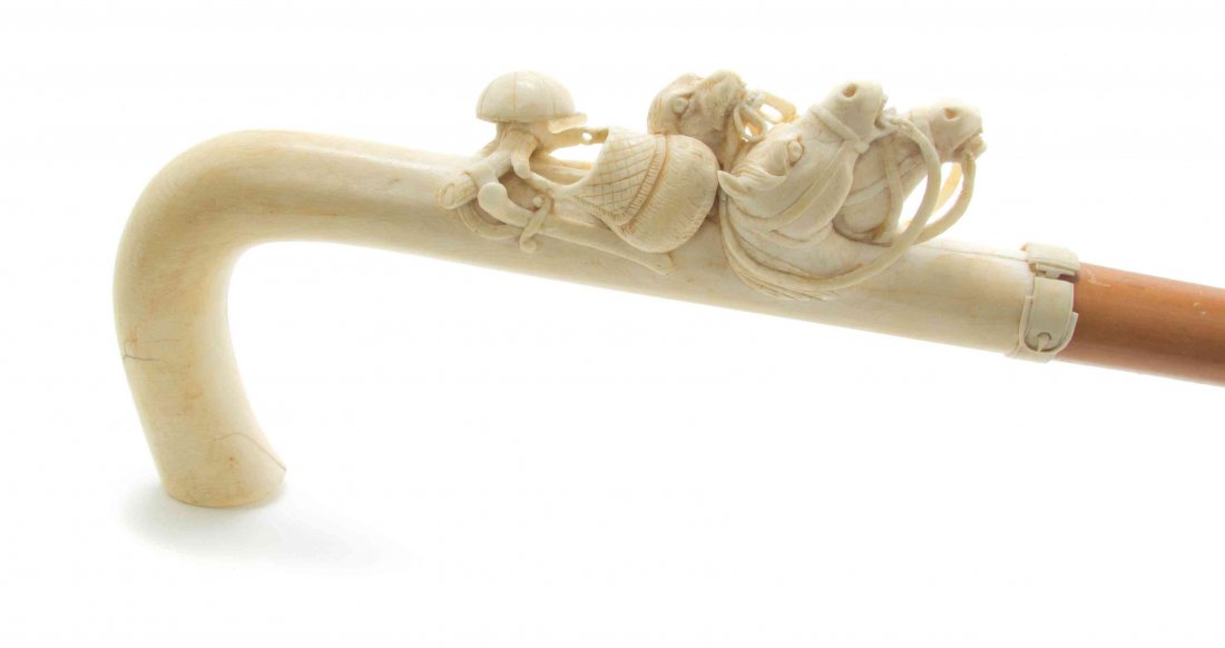 A Continental Relief Carved Ivory Cane, Height of: A Continental Relief Carved Ivory Cane, having an L-form handle with decoration relating to the hunt, including a cap, knife and scabbard, bag, hound's head and two horse heads ending in a belt carved