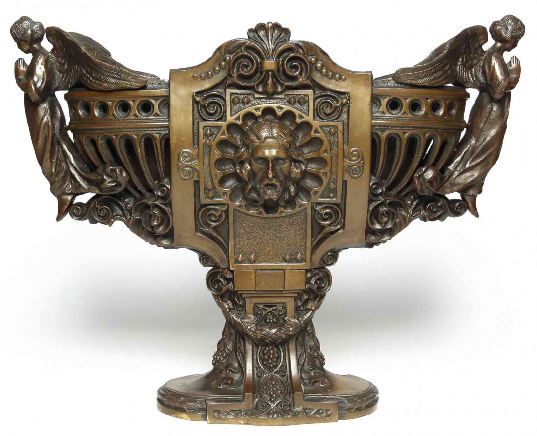 A Continental Cast Metal Jardiniere, Width over handles: A Continental Cast Metal Jardiniere, having a mask of Christ upon a gothic Catherine window, with handles at each end in the form of angels. Width over handles 20 inches. Property from the Collection 
