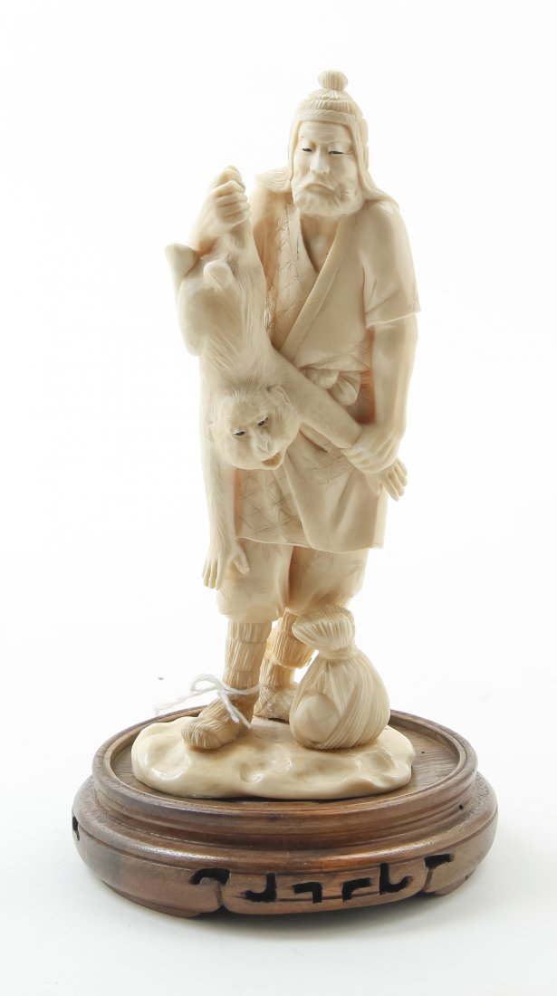 A Japanese Carved Ivory Figure of a Man Catching a: A Japanese Carved Ivory Figure of a Man Catching a Monkey, the figure holding the creature by its back legs Height overall 7 1/4 inches.