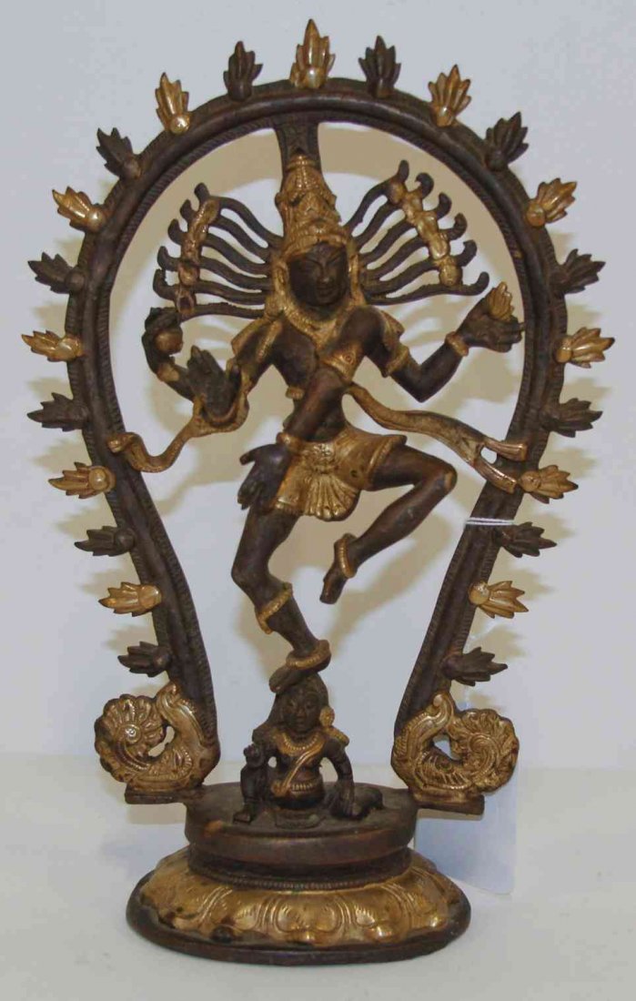 An Indian Partial Gilt Bronze Multi-Armed Deity, Height: An Indian Partial Gilt Bronze Multi-Armed Deity, depicted standing upon a smaller figure within a horseshoe-form mandorla and raised on a waisted circular base. Height 11 5/8 inches.