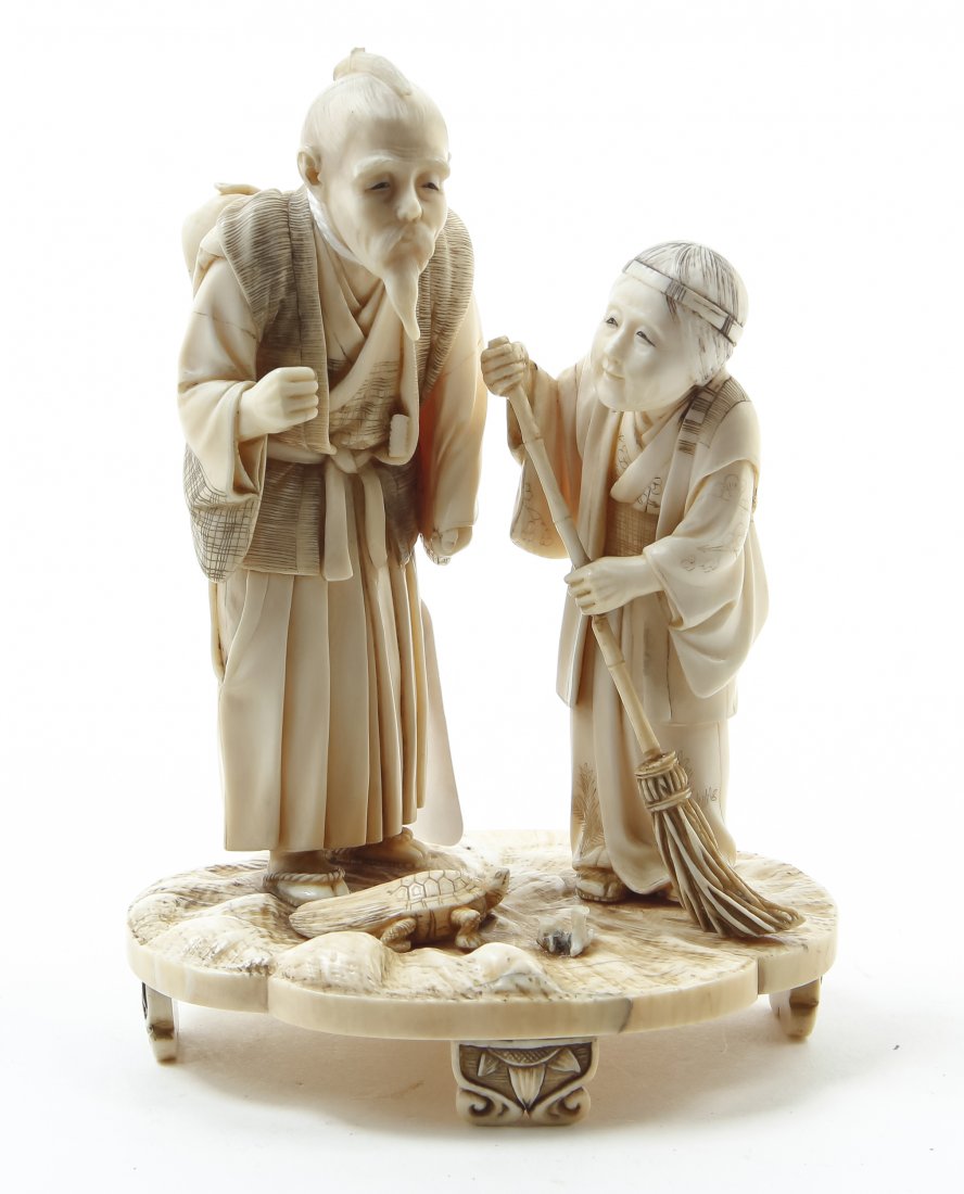 A Japanese Carved Ivory Okimono, Height 5 1/4 inches.: A Japanese Carved Ivory Okimono, depicting an elderly peasant couple, the lady with a broom, both figures depicted standing upon a naturalistic base with a magic turtle at their feet, having a red inl