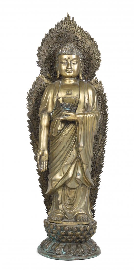 A Gilt Metal Figure of Buddha, Height 34 1/2 inches.: A Gilt Metal Figure of Buddha, depicting standing and backed by a flame-form mandorla, with the Wan symbol on his chest and holding a lotus blossom in one palm, raised on a lotus-form base. Height 34 