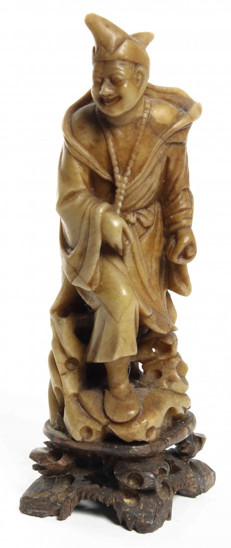 A Carved Soapstone Figure, Height 7 3/4 inches.: A Carved Soapstone Figure, depicting a robed figure in hat, raised on a carved wood base. Height 7 3/4 inches.