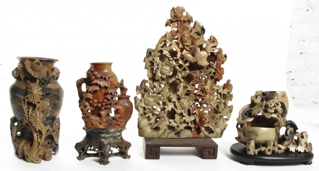 A Group of Four Chinese Soapstone Carvings, Height of: A Group of Four Chinese Soapstone Carvings, comprising vessels amongst foliage compositions, two raised on a wood stand, one raised on a soapstone stand. Height of tallest 12 1/4 inches. Property from