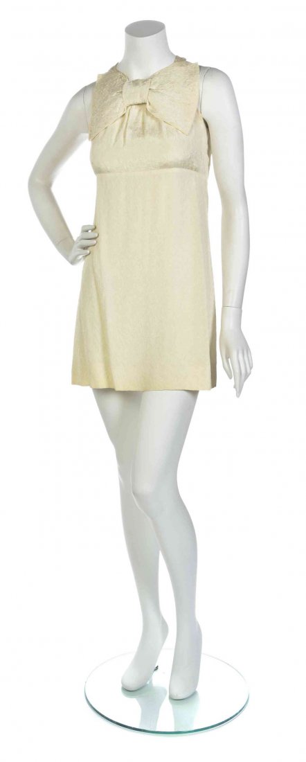 A Pierre Cardin Ivory Satin Matelasse Dress,: A Pierre Cardin Ivory Satin Matelasse Dress, sleeveless with an oversized bow to the collar and an empire waist. Labeled: Pierre Cardin "Jeunesse" Paris.