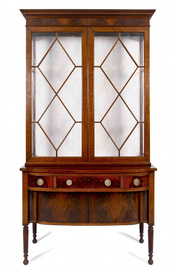 A Regency Style Mahogany Display Cabinet, Height 82 3/4: A Regency Style Mahogany Display Cabinet, in two parts, the upper section with molded cornice over two navette-shaped astragal doors, the lower section with bow front top over a long drawer flanked by