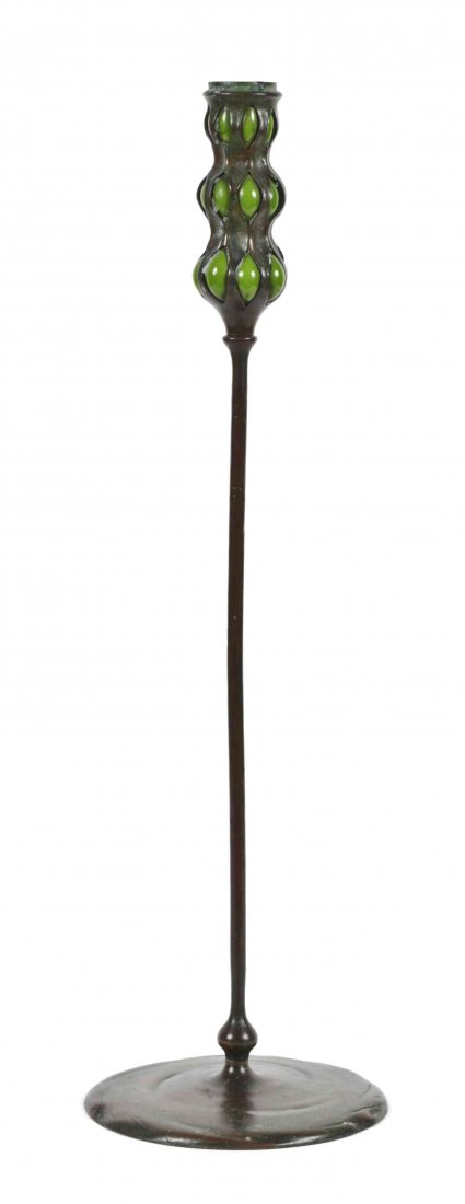 A Tiffany Studios Bronze and Favrile Glass Candlestick,: A Tiffany Studios Bronze and Favrile Glass Candlestick, the three part candlecup with green blown-out glass, over a cylindrical standard, raised on a circular foot, stamped Tiffany Studios New York, n