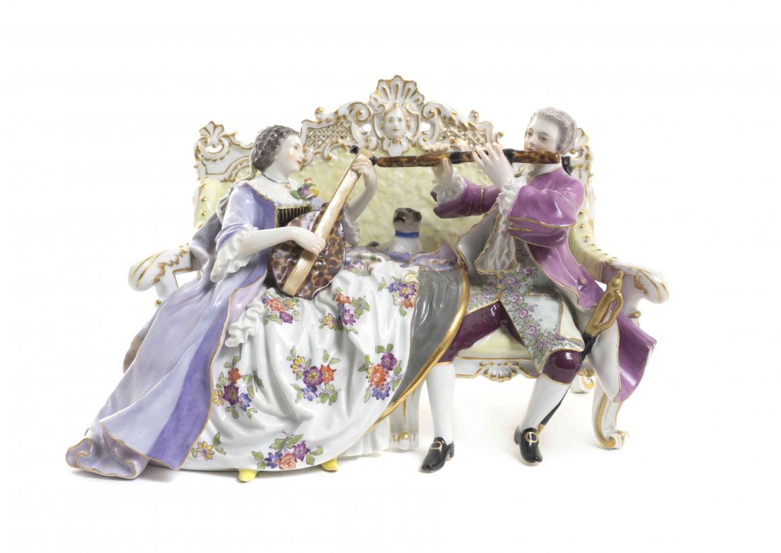 A Meissen Porcelain Figural Group, Width 9 1/4 inches.: A Meissen Porcelain Figural Group, depicting a lady and a gentleman musician with a pug seated on a settee, having crossed swords in underglaze blue, incised W56 and impressed 13. Width 9 1/4 inches. 