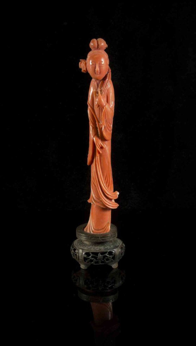A Carved Coral Figure of a Lady, Height 4 1/2 inches.: A Carved Coral Figure of a Lady, of a rich salmon pink, the figure depicted standing and holding a flower, with a looped coiffure above her round face, the carving showing strands of her hair and plea