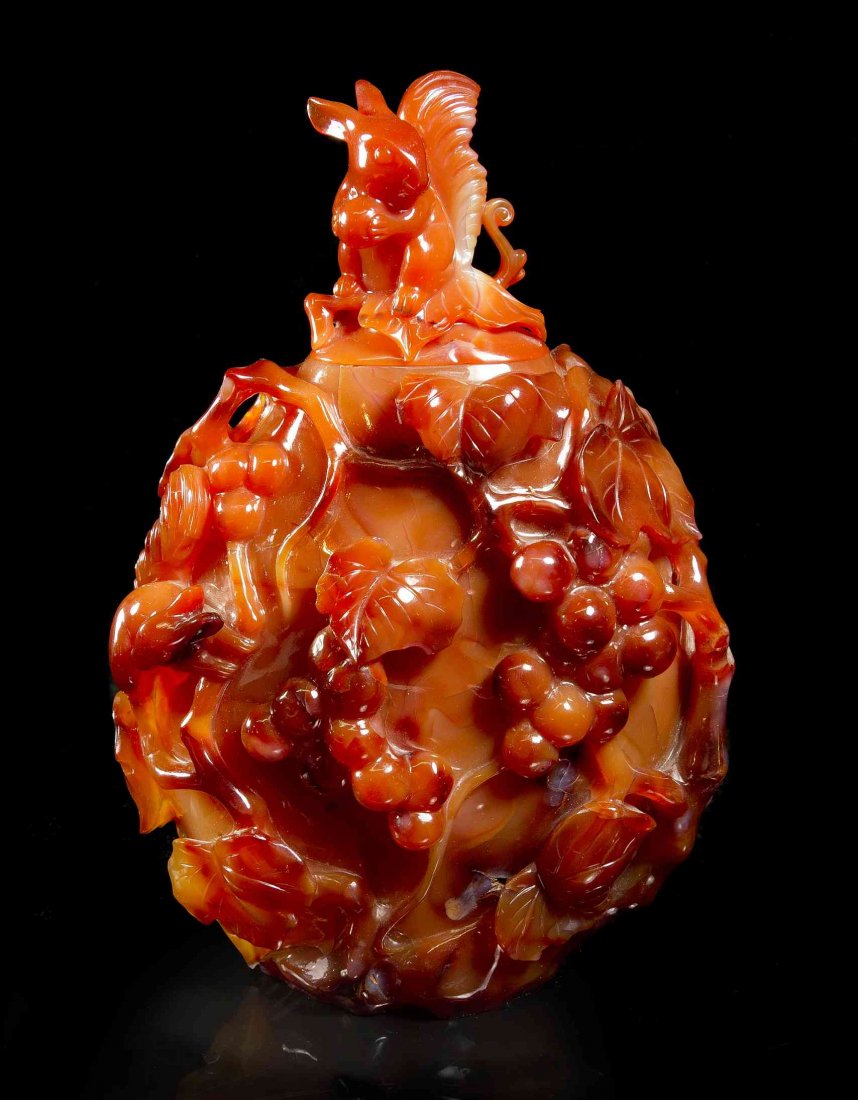 A Chinese Carved Carnelian Covered Urn, Height 7 3/4: A Chinese Carved Carnelian Covered Urn, the cover surmounted with a squirrel form finial, the body of ovoid form and depicting fruiting, flowering leafy branches, with high polish and raised on a fitt