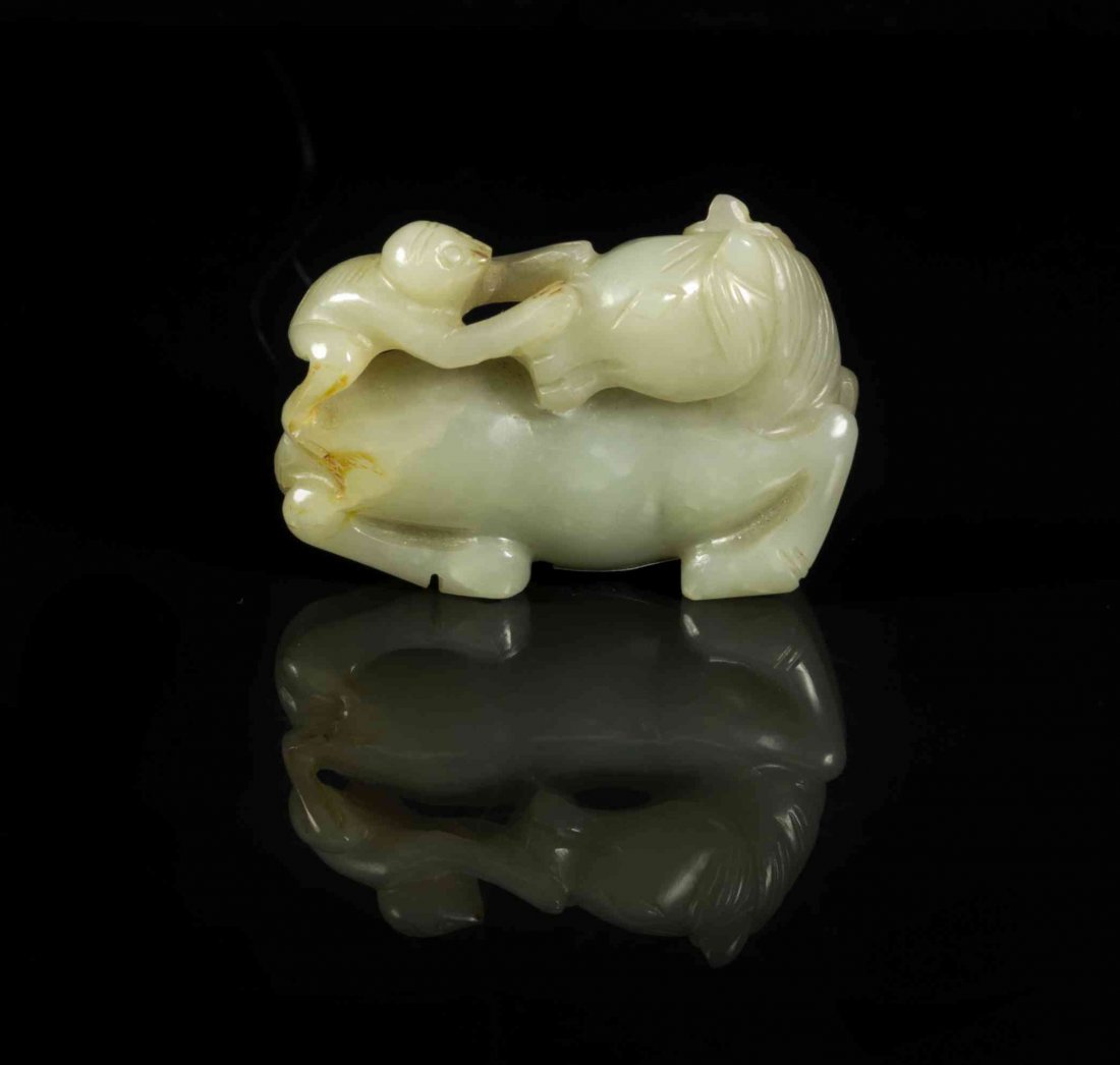 A Carved Jade Toggle of a Horse, Width 2 1/4 inches.: A Carved Jade Toggle of a Horse, of a mottled celadon colored stone with a light russet skin, the horse depicted recumbent, its head craned around towards the monkey clambering on its back. Width 2 1/