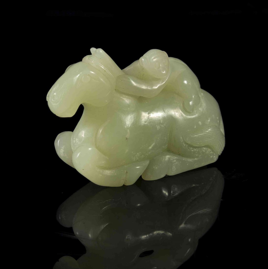 A Carved Jade Toggle of a Monkey Riding a Horse, Width: A Carved Jade Toggle of a Monkey Riding a Horse, of a pale celadon colored stone, the horse depicted recumbent with its legs folded beneath itself, the monkey grasping the horse's mane. Width 2 1/4 in