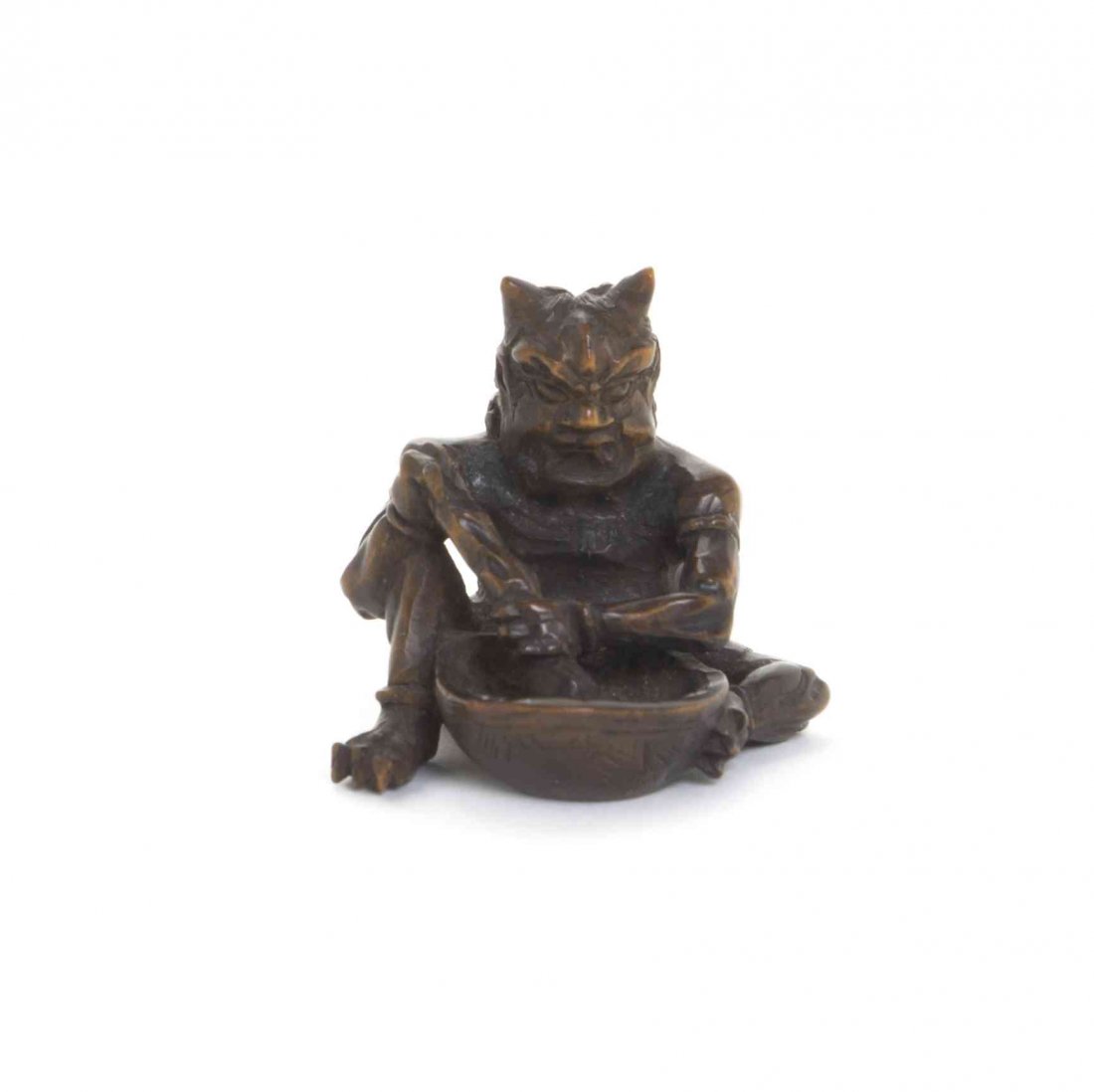 A Carved Wood Oni Netsuke, Width at widest 1 1/2: A Carved Wood Oni Netsuke, the figure depicted seated at work with mortar and pestle. Width at widest 1 1/2 inches.