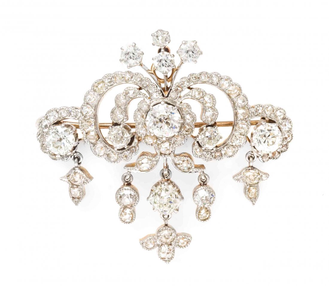 An Edwardian Platinum Topped Gold and Diamond: An Edwardian Platinum Topped Gold and Diamond Pendant/Brooch, in a scrolling openwork design suspending containing one old European cut diamond weighing approximately 1.15 carats, one old mine cut dia