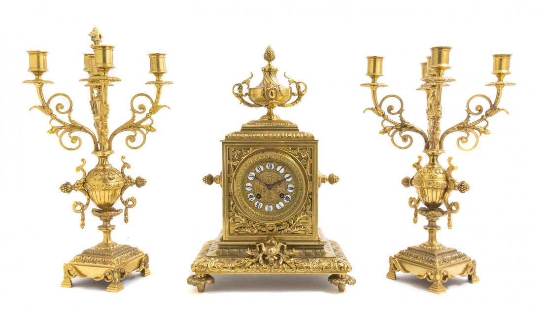 A French Gilt Bronze Three-Piece Clock Garniture,: A French Gilt Bronze Three-Piece Clock Garniture, comprising a clock and a pair of five-light baluster form candelabra, the clock surmounted with an urn form finial over the rectangular case set with 