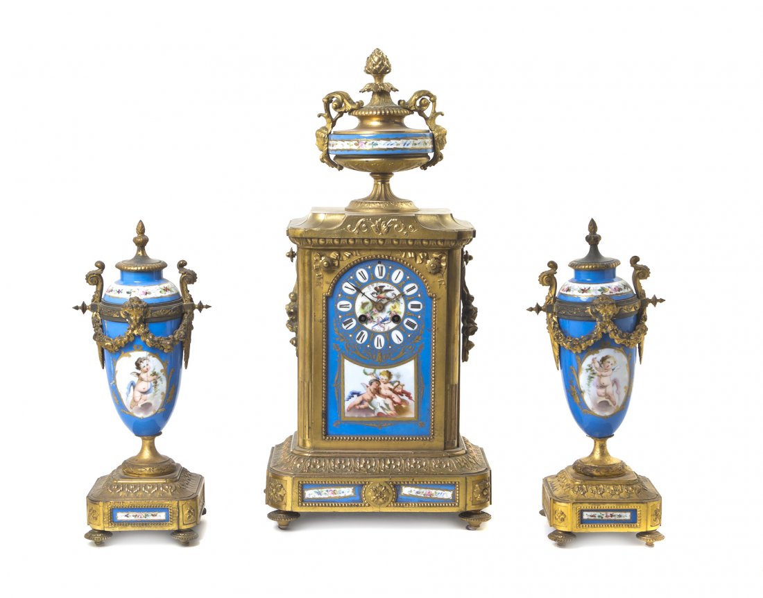 A Louis XVI Style Gilt Bronze Mounted Porcelain Clock: A Louis XVI Style Gilt Bronze Mounted Porcelain Clock Garniture, LATE 19TH CENTURY, MOVEMENT BY JAPY FRERES, PARIS, having a shaped clock case set with a porcelain plaque painted to show a circular di