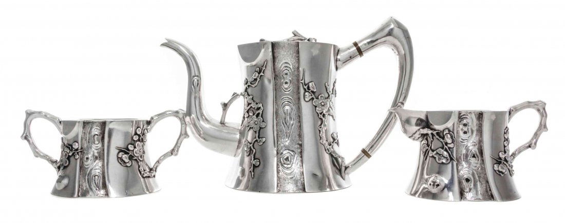 A Chinese Export Silver Three-Piece Tea Set, Height of: A Chinese Export Silver Three-Piece Tea Set, Lue Wo, Shanghai, Circa 1900, comprising a teapot, creamer, and sugar bowl, of paneled spool form, the sides chased with panels of faux bois and applied wi