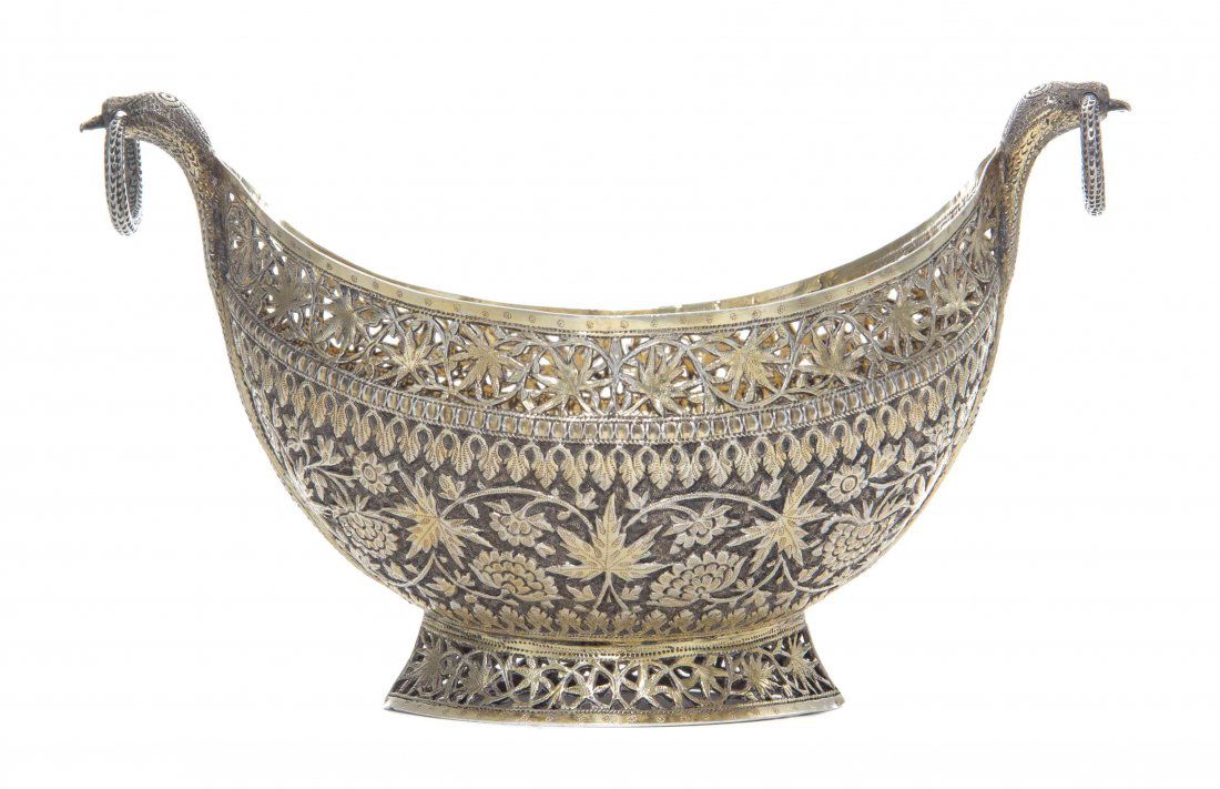 An Indian Silver-Gilt Bowl, Length over handles 8 3/4: An Indian Silver-Gilt Bowl, Circa 1900, of oval boat form, the body densely chased with flowers and foliage against a matted ground below a band of openwork scrolling foliage, raised on a conforming p