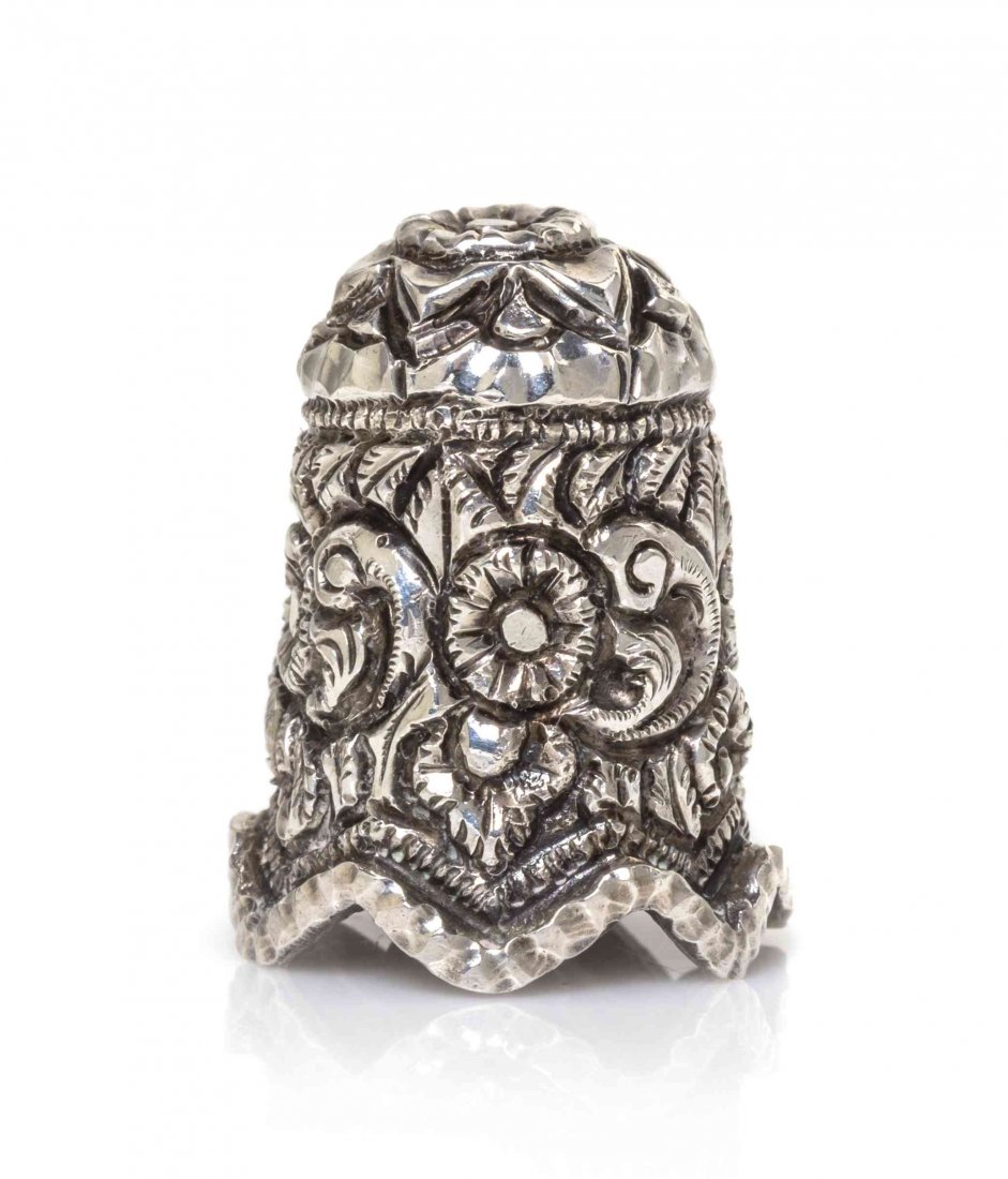 An Indian Silver Thimble, Height 1 15/16 inches.: An Indian Silver Thimble, LATE 19TH CENTURY, embossed and chased overall in high relief with flowers and scrolling foliage, the top with a large flower head, having a scalloped rim, apparently unmarke