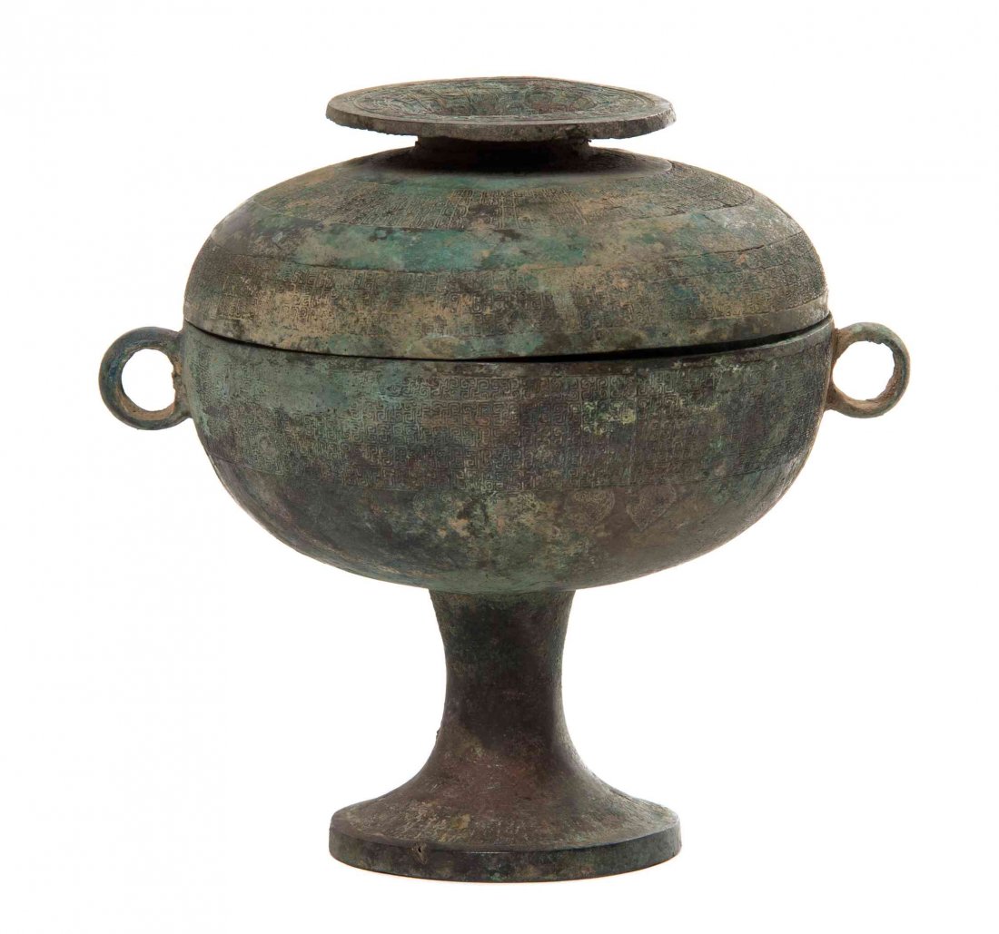 An Archaistic Bronze Dou Vessel Height 8 1/4 inches.: An Archaistic Bronze Dou Vessel the circular covered food vessel raised on a pedestal foot and flanked by loop handles, with a disc-form finial elevated above the domed cover, having relief decoration