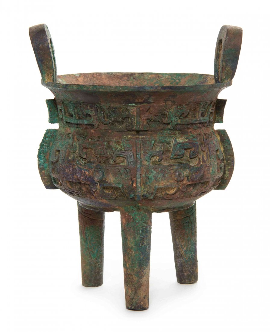 A Bronze Tripod Li Ding, Height over handles 11 inches.: A Bronze Tripod Li Ding, the round bowl surmounted with two upright loop handles, the recessed neck having raised flanges separating sinuous beasts in relief above a the body decorated with taotie and