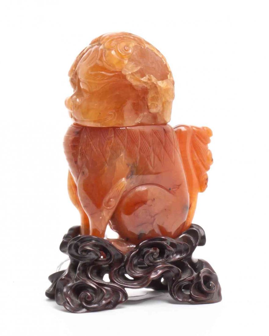 A Chinese Carved Carnelian Lion Form Bottle, Height of: A Chinese Carved Carnelian Lion Form Bottle, raised on a carved wood stand. Height of bottle 4 inches. Condition: The figure having a loss to head, as shown in photograph.