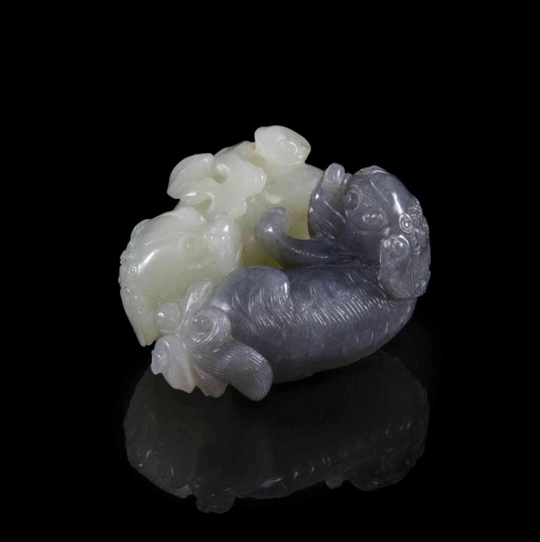 A Greyish-Lavender and White Jade Carved Toggle, Width: A Greyish-Lavender and White Jade Carved Toggle, depicting two lions carved in opposing recumbent poses. Width 2 1/8 inches. Condition: In overall good complete condition, with minor wear throughout.