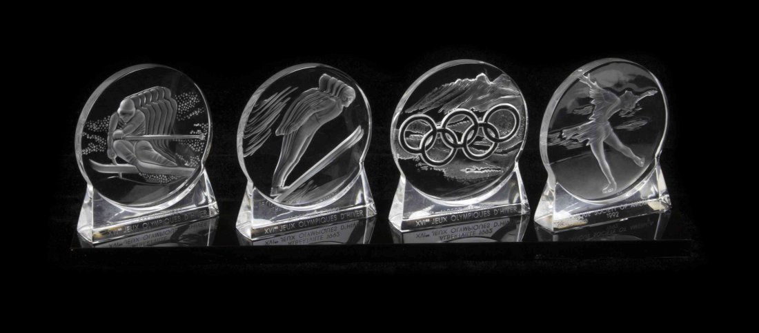 A Set of Four Lalique Molded and Frosted Glass: A Set of Four Lalique Molded and Frosted Glass Commemorative Roundels, depicting the 1992 Olympic Winter Games, raised on a black lucite base, etched Lalique R France, three numbered 224 of 4000. Heig