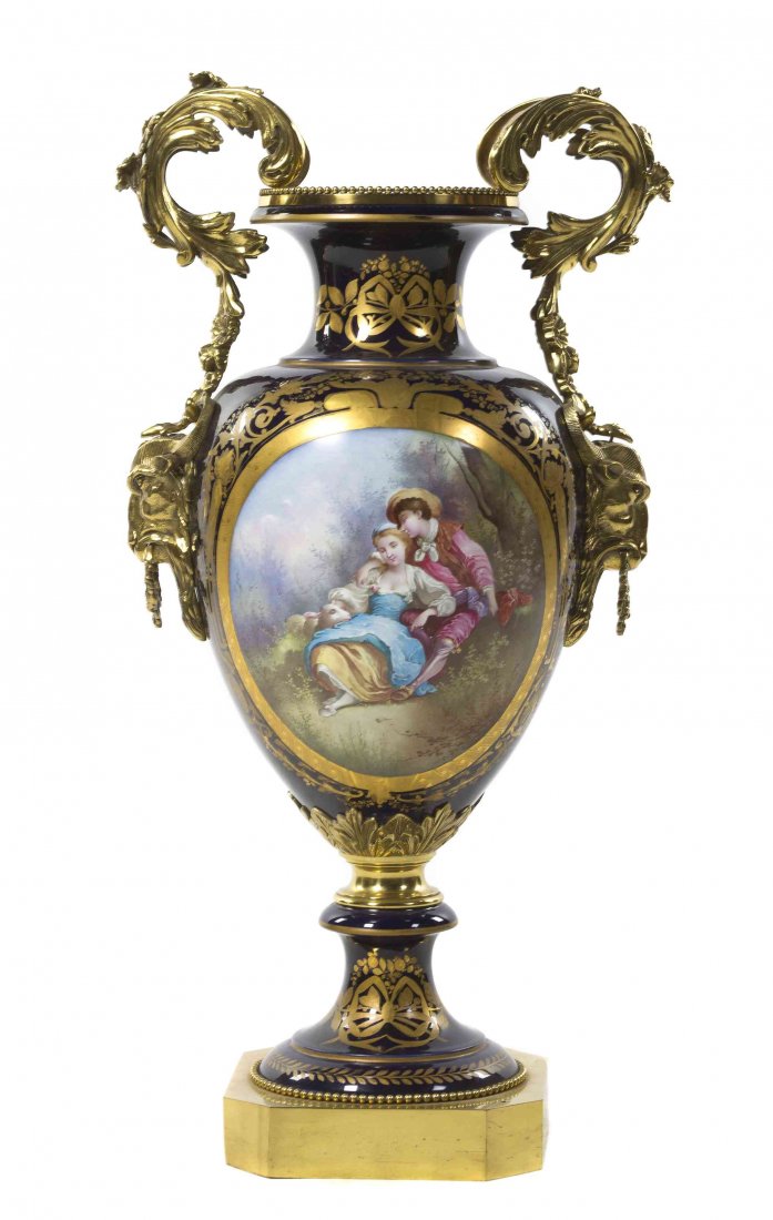 A Sevres Style Gilt Bronze Mounted Porcelain Urn,: A Sevres Style Gilt Bronze Mounted Porcelain Urn, of baluster form with foliate handles terminating in ram masks, the cobalt body painted with a scene depicting a shepherd and a shepherdess signed Gug