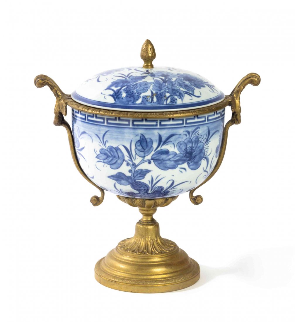 A Continental Bronze Mounted Porcelain Urn, Height: A Continental Bronze Mounted Porcelain Urn, of circular form having a domed lift off cover with a berry finial, mounted at the shoulders with foliate scroll handles, raised on a circular foot. Height