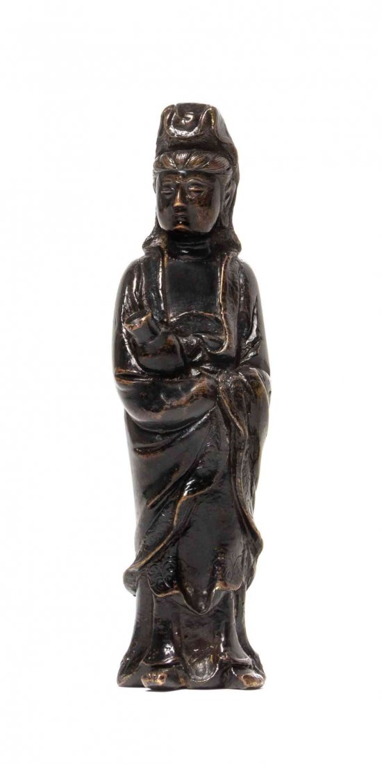 A Chinese Bronze Figure of Guanyin, Height 6 3/4: A Chinese Bronze Figure of Guanyin, having a lacquer finish, the deity depicted standing in draped robes and cradling a bottle, with scrolling lotus decoration to her garments. Height 6 3/4 inches. Co