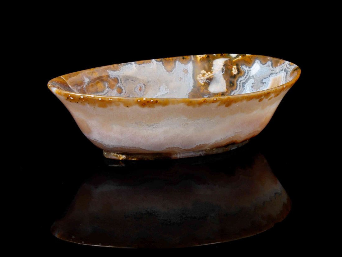 A Carved Agate Bowl,, , the translucent banded agate: A Carved Agate Bowl, the translucent banded agate showing a range of color ranging from rich brown to black to light grey in a complex swirling pattern. 21.84 x 11.80 x 6.10 cm. Property from the Esta