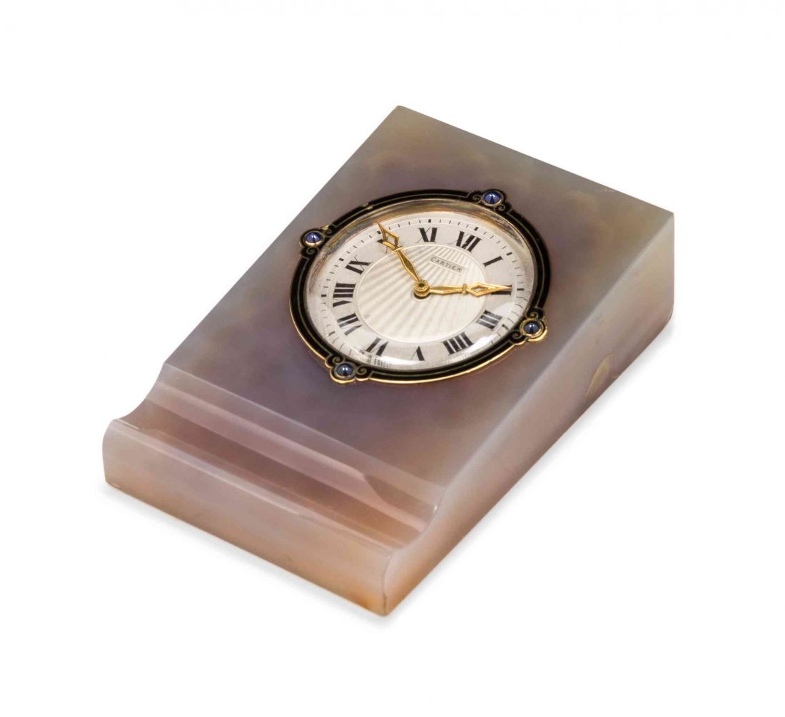 An Art Deco Gold, Sapphire, Enamel and Agate Desk Clock: An Art Deco Gold, Sapphire, Enamel and Agate Desk Clock Set, Cartier Paris, Circa 1920, consisting of a wedge form carved translucent grey agate base with grooved pen rest inset with a circular clock,