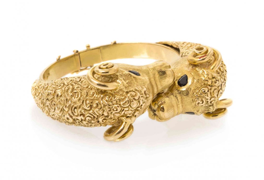 An 18 Karat Yellow Gold and Sapphire Ram's Head Bypass: An 18 Karat Yellow Gold and Sapphire Ram's Head Bypass Bangle, J Rossi, consisting of two ram's heads with textured finish and four pear shaped sapphires. Stamp: 18K (J Rossi). 62.90 dwts. Property fr