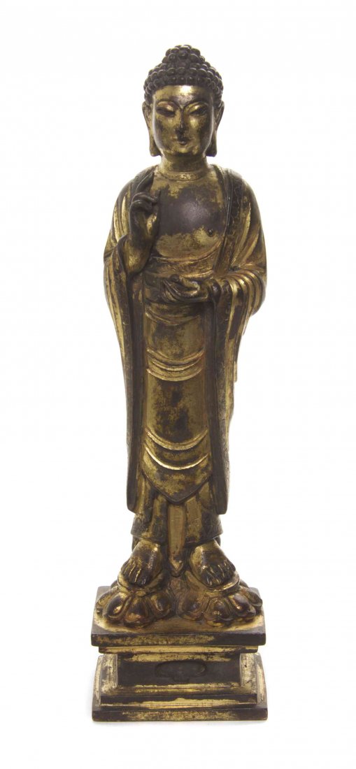 A Gilt Bronze Model of a Standing Buddha, Height: A Gilt Bronze Model of a Standing Buddha, the deity depicted with a soft, downward cast gaze and in draped robes, raised on a squared pedestal base. Height overall 11 3/8 inches.