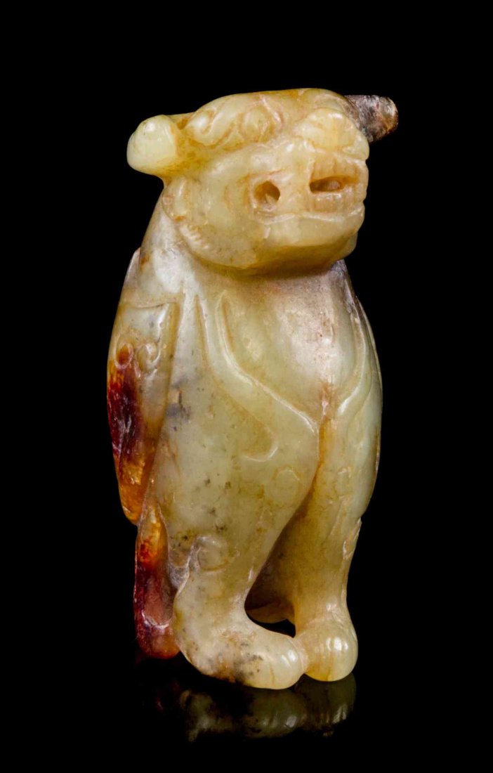 A Carved Jade Toggle, Height 2 inches.: A Carved Jade Toggle, of a yellow and russet stone with red skin, the beast depicted with scrolled horns, tapering ears and fangs, with a winged body and paws, having relief carved detail and a beast 