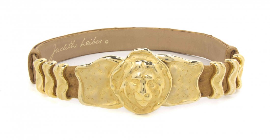 A Judith Leiber Tan Ostrich Leather Belt, 25 inches.: A Judith Leiber Tan Ostrich Leather Belt, adjustable, with a goldtone lion's head buckle. Stamped: Judith Leiber. 25 inches. Condition: Overall very good condition. Please note the following: Scratchi