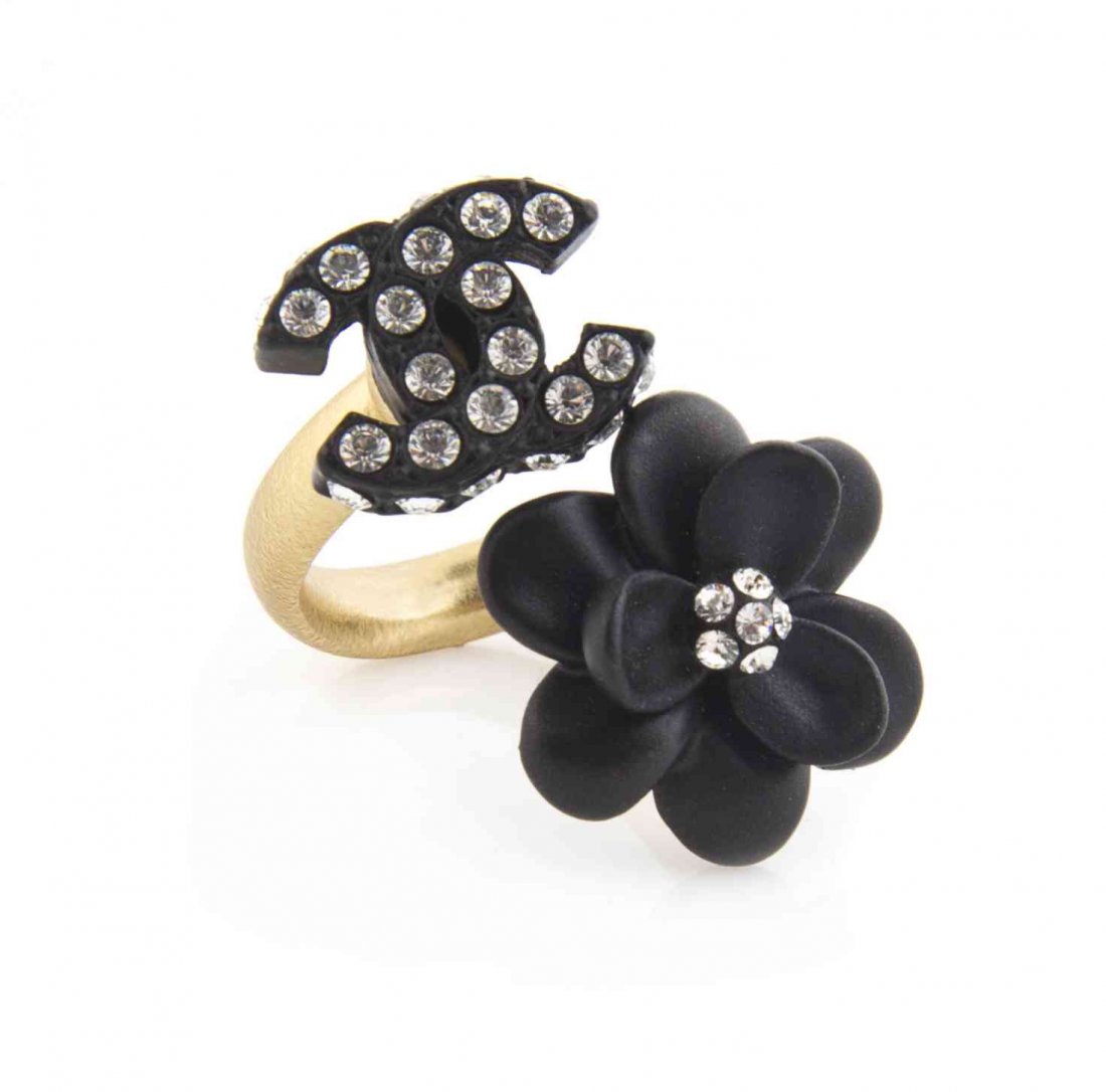 A Chanel Goldtone Black Camellia Ring,: A Chanel Goldtone Black Camellia Ring, with an attached rhinestone interlocking 'C' logo. Stamped: Chanel. Condition: Overall very good condition. Comes with box.