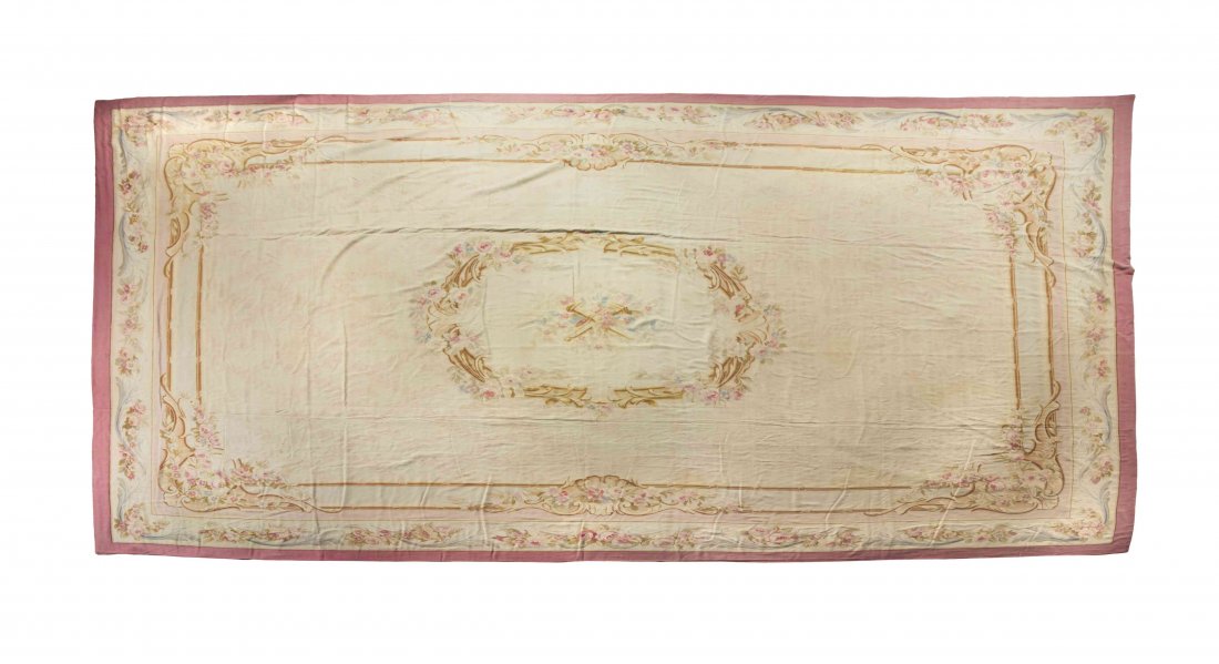 An Aubusson Wool Rug, 20 feet 9 inches x 13 feet 6: An Aubusson Wool Rug, having a torch and quiver trophy within a central cartouche on an ivory ground within multiple shell and floral borders. 20 feet 9 inches x 13 feet 6 inches.