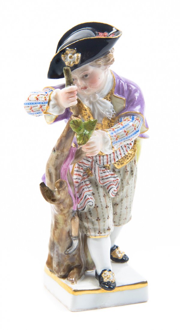 A Meissen Porcelain Figure, Height 3 7/8 inches.: A Meissen Porcelain Figure, depicting a boy in eighteenth century attire carving a tree, with crossed swords in underglaze blue and various impressed and incised marks. Height 3 7/8 inches.