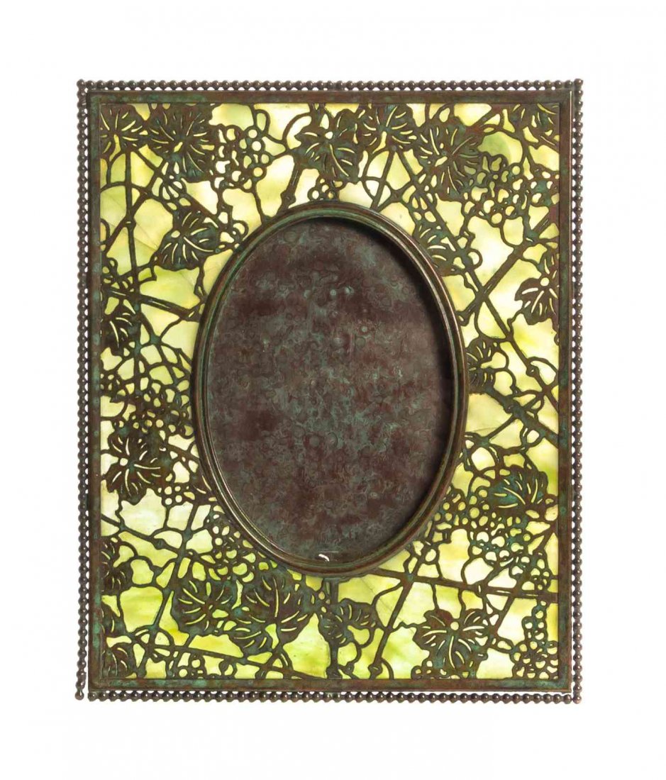 A Tiffany Studios Bronze and Favrile Glass Picture: A Tiffany Studios Bronze and Favrile Glass Picture Frame, in the Grapevine pattern, with green slag glass, stamped Tiffany Studios New York. Height 10 inches. Condition: Frame in decent stable conditi