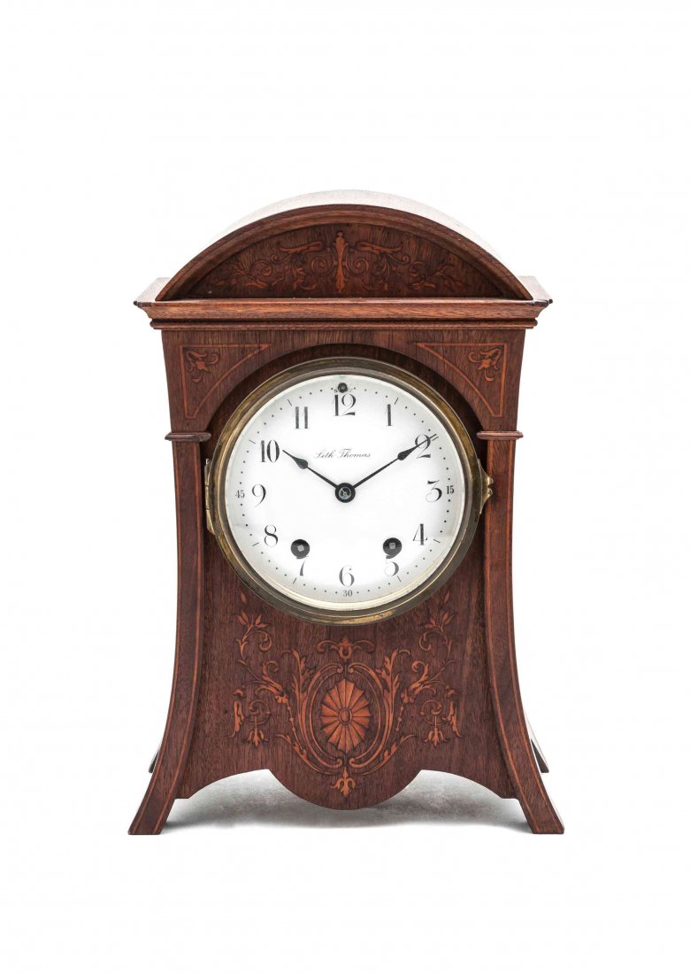 A Seth Thomas Mantel Clock, Height 13 3/8 inches.: A Seth Thomas Mantel Clock, 19th century, the arched crest over the conforming case with sloped sides having scrolling foliate inlay to the front and centered with a circular clock face, raised on sho