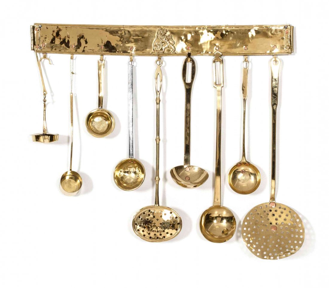 A Collection of Nine Brass Kitchen Utensils, Length of: A Collection of Nine Brass Kitchen Utensils, comprising ladles, strainers and serving articles, with wall-mounted hanging display. Length of longest 21 1/2 inches.