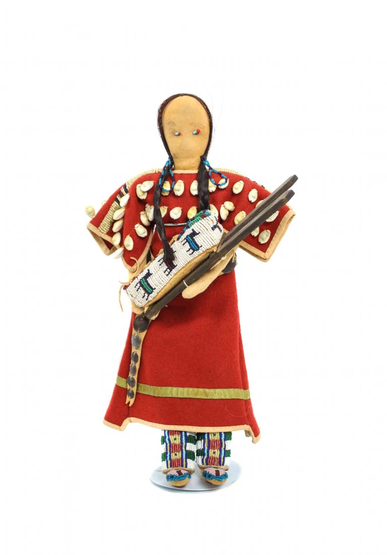 A Contemporary Cheyenne Doll, Height 14 inches.: A Contemporary Cheyenne Doll, having red flannel dress with cowrie shells on yoke, beaded on shoulders, a plains style concha belt, beaded leggings and moccasins, holding a pictorial cradle containing