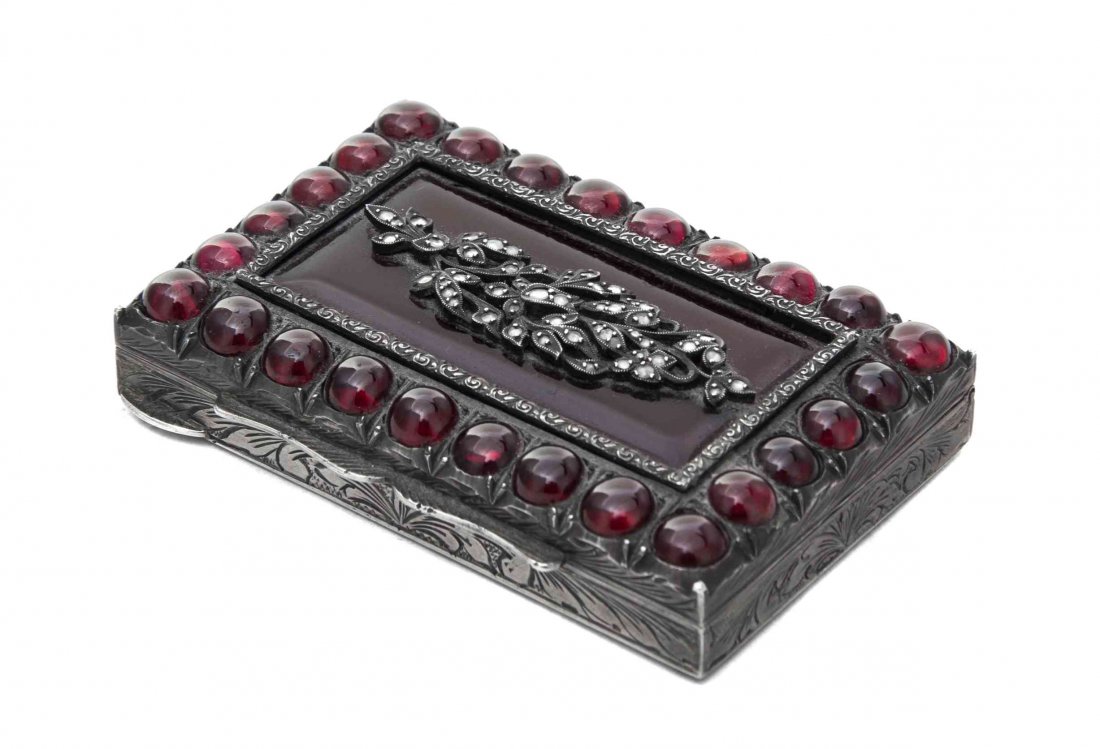 A Diamond, Garnet and Glass-Mounted Silver Snuff Box,: A Diamond, Garnet and Glass-Mounted Silver Snuff Box Late 19th Century the sides and base of the rectangular body engraved with scrolling foliage, the hinged cover bordered with twenty-six cabochon ga