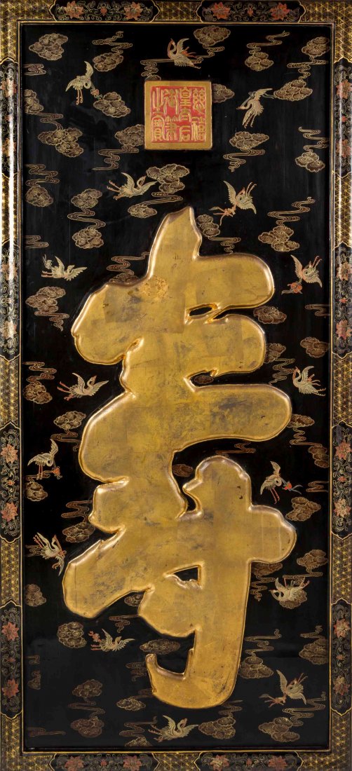 A Chinese Lacquered Panel, Height 87 1/2 x width 40: A Chinese Lacquered Panel, having raised gilt-painted shou, on a black ground with cranes and beribboned Buddhist and Daoist emblems, with a carved seal mark and florally decorated borders. Height 87 