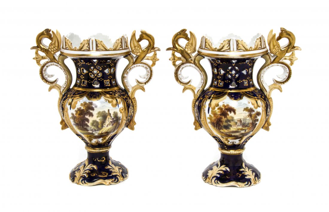A Pair of Continental Porcelain Urns, Height 8 3/4: A Pair of Continental Porcelain Urns, each of baluster form mounted at the shoulders with dragon form handles, the body painted to show an architectural cartouche raised on a foliate decorated foot. H
