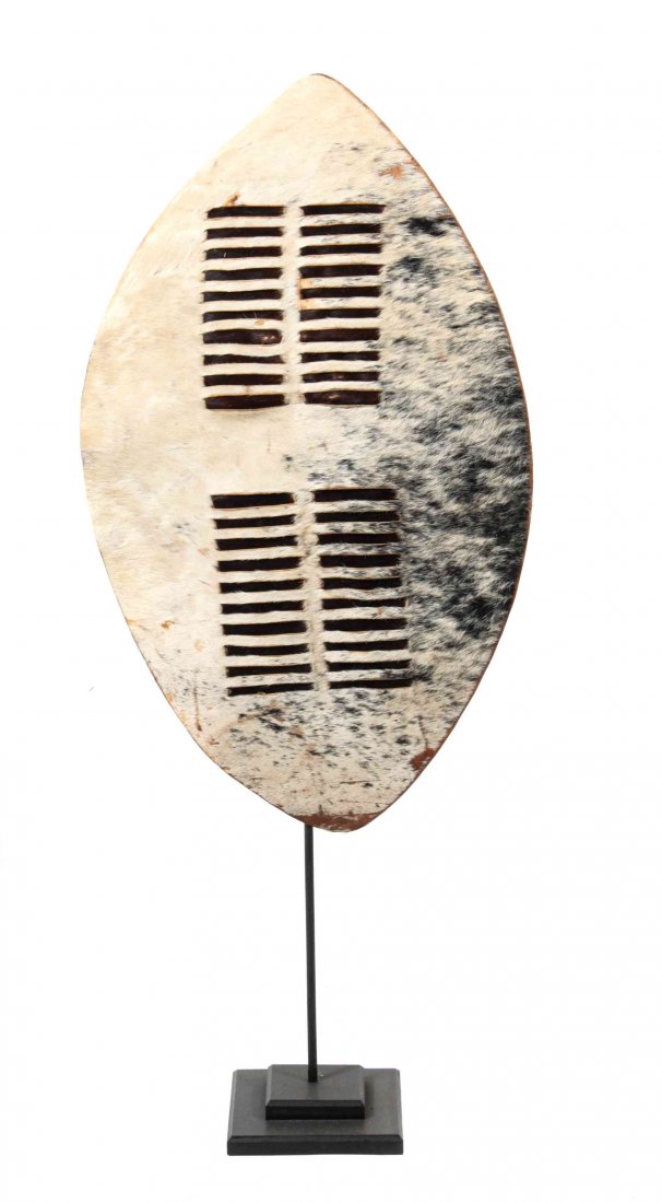 An African Zulu Style Animal Hide Shield, Height 26 x: An African Zulu Style Animal Hide Shield, the grey and cream patched hide interlaced with securing strips, with leather strap handle to verso. Height 26 x width 15 inches. Property from the Estate of 