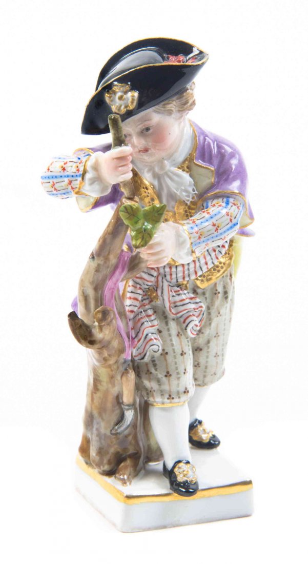 A Meissen Porcelain Figure Height 3 7/8 inches.: A Meissen Porcelain Figure depicting a boy in eighteenth century attire carving a tree, with crossed swords in underglaze blue and various impressed and incised marks. Height 3 7/8 inches.