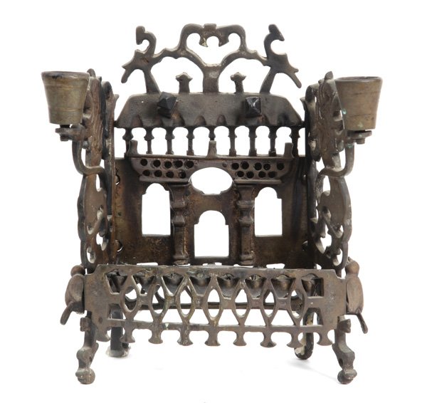 Hanukkah Lamp – Poland: Hanukkah lamp. Poland, [first half of 20th cent.]. Cast brass. Back-plate designed as a front of a building with a gate, windows and a balcony. Side-plates in the shape of lions. From these plates eme
